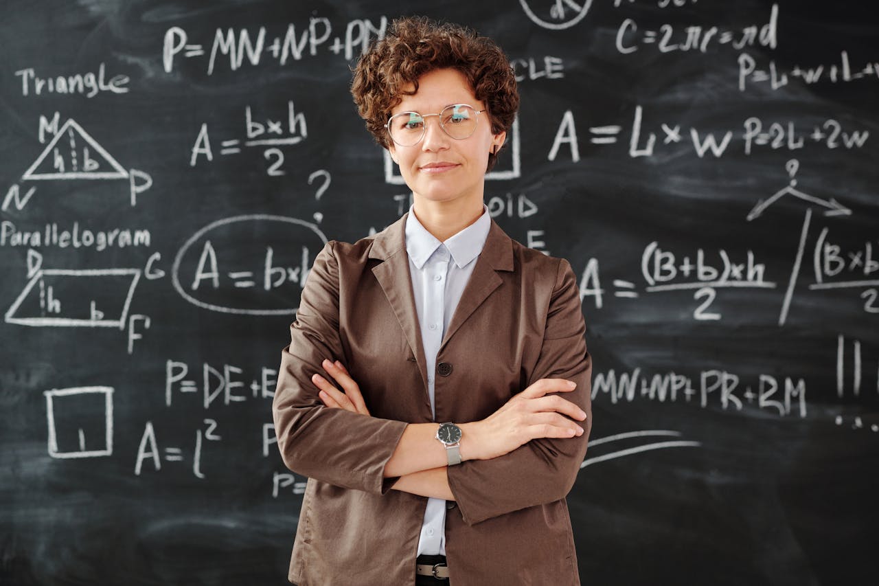 Services Confident female teacher standing with arms crossed in front of a detailed mathematical blackboard.